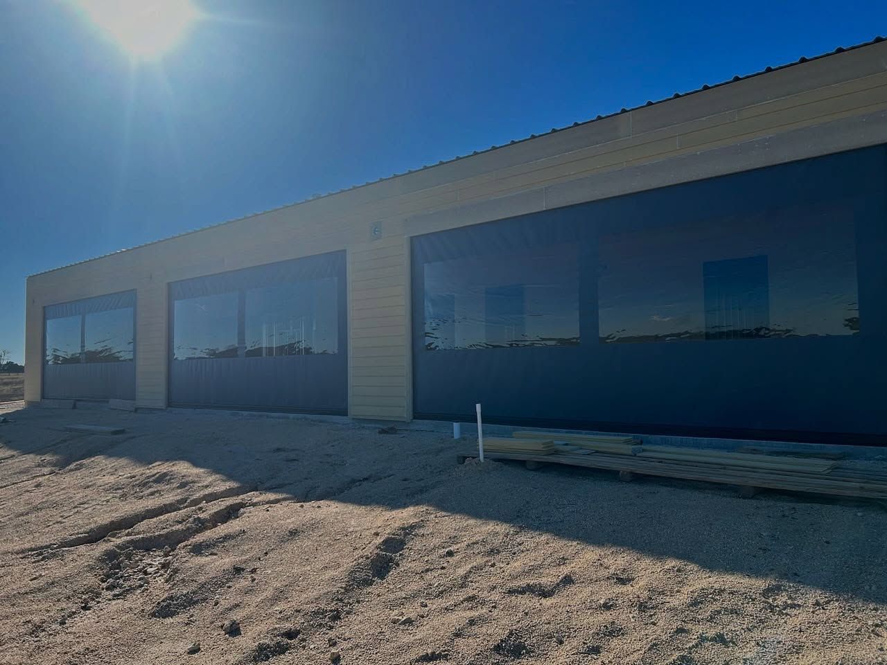 Building with large, dark-tinted windows, tan siding, and a bright blue sky.