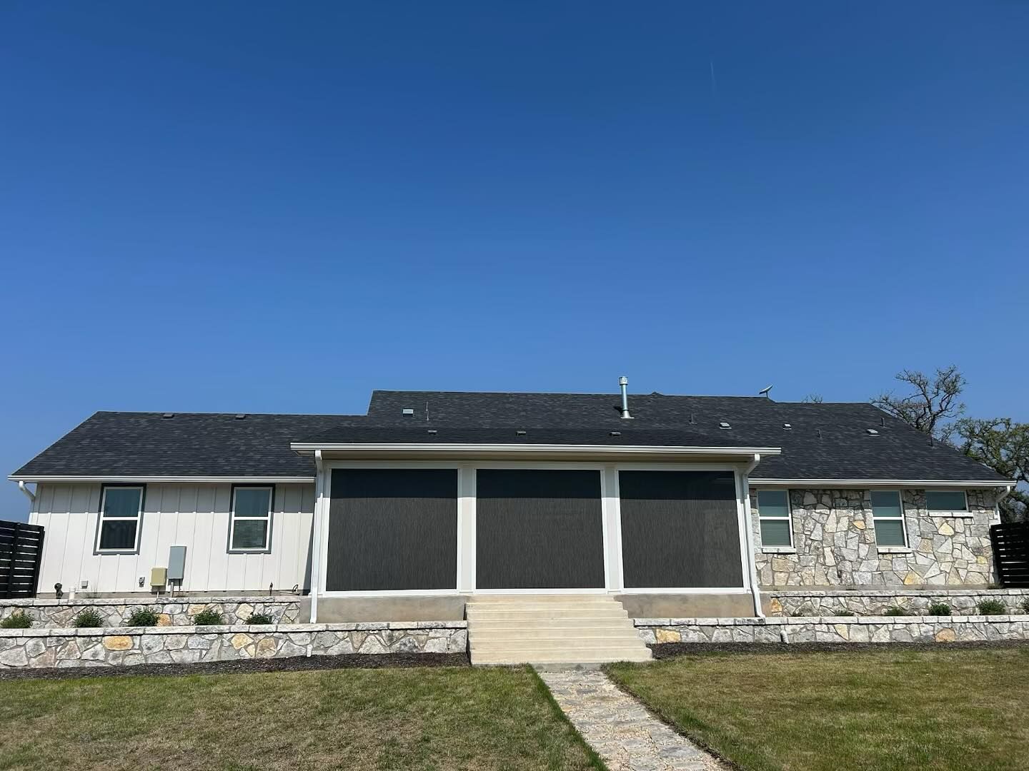 Back view of a house with a dark roof, stone and white siding, screened patio, and a blue sky.