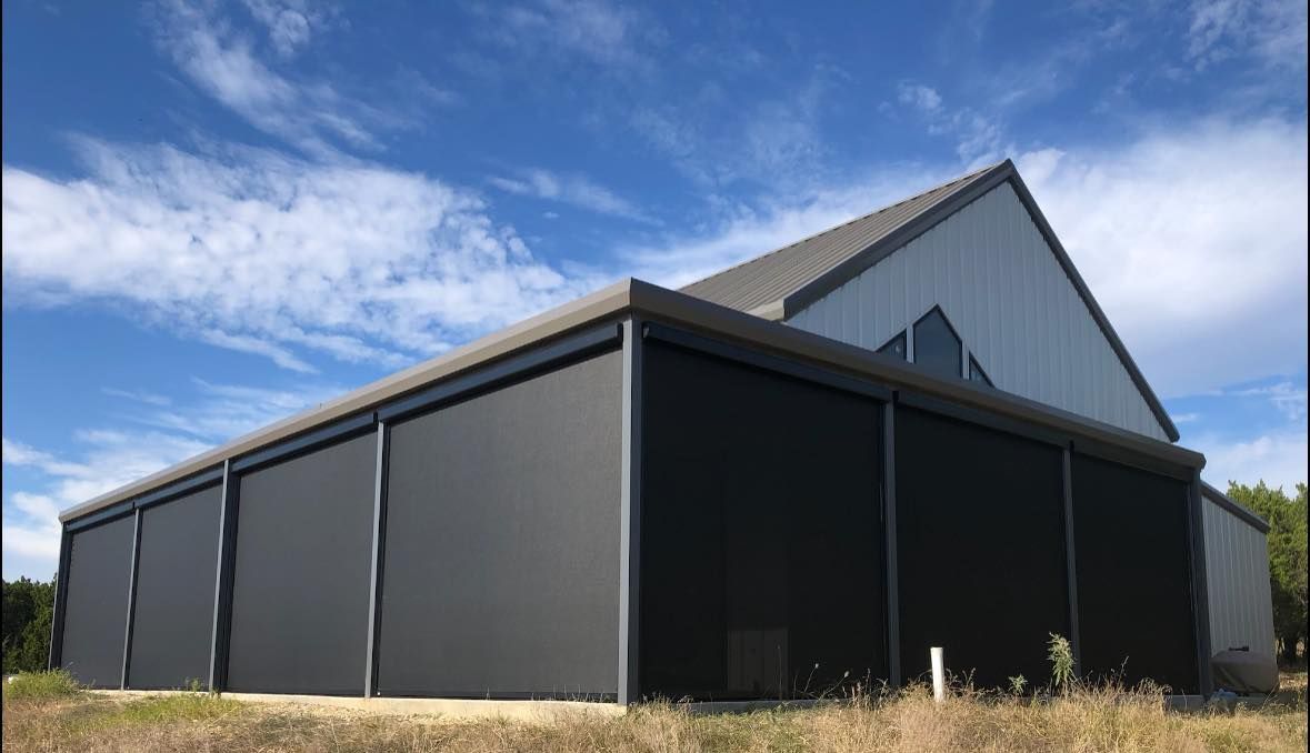 Dark gray building with large roll-down shades under a cloudy blue sky.