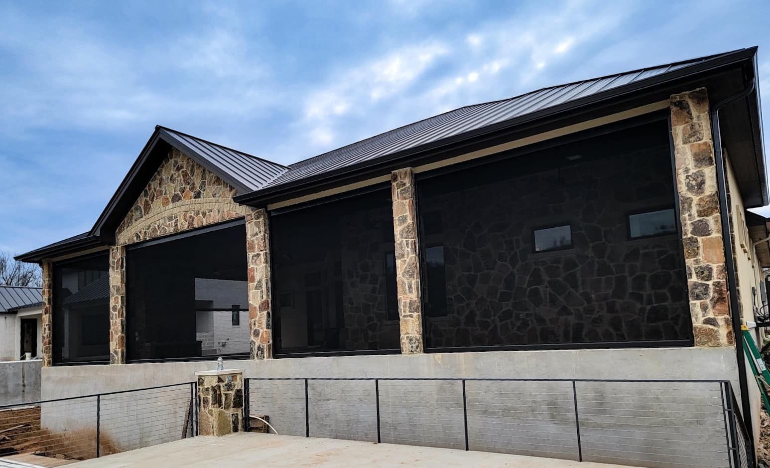 Two-story building with stone and black siding, dark roof, and garage-style opening under a cloudy sky.