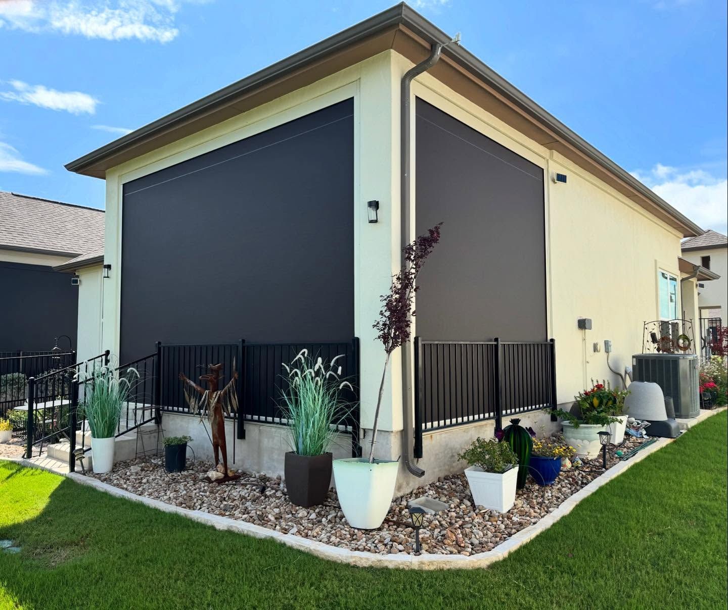 Exterior of a house with two large black outdoor shades, surrounded by landscaping and a black railing.