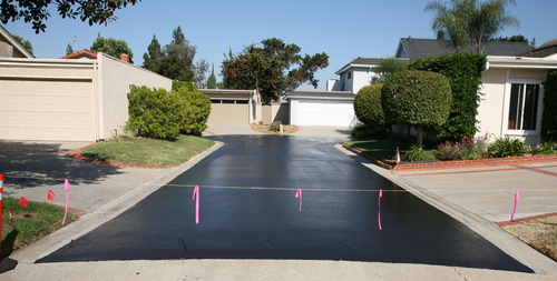 Paved driveway leading to multiple garages between houses under a clear blue sky.