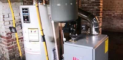 A water heater and furnace are in a brick-walled basement. Metal pipes are connected.
