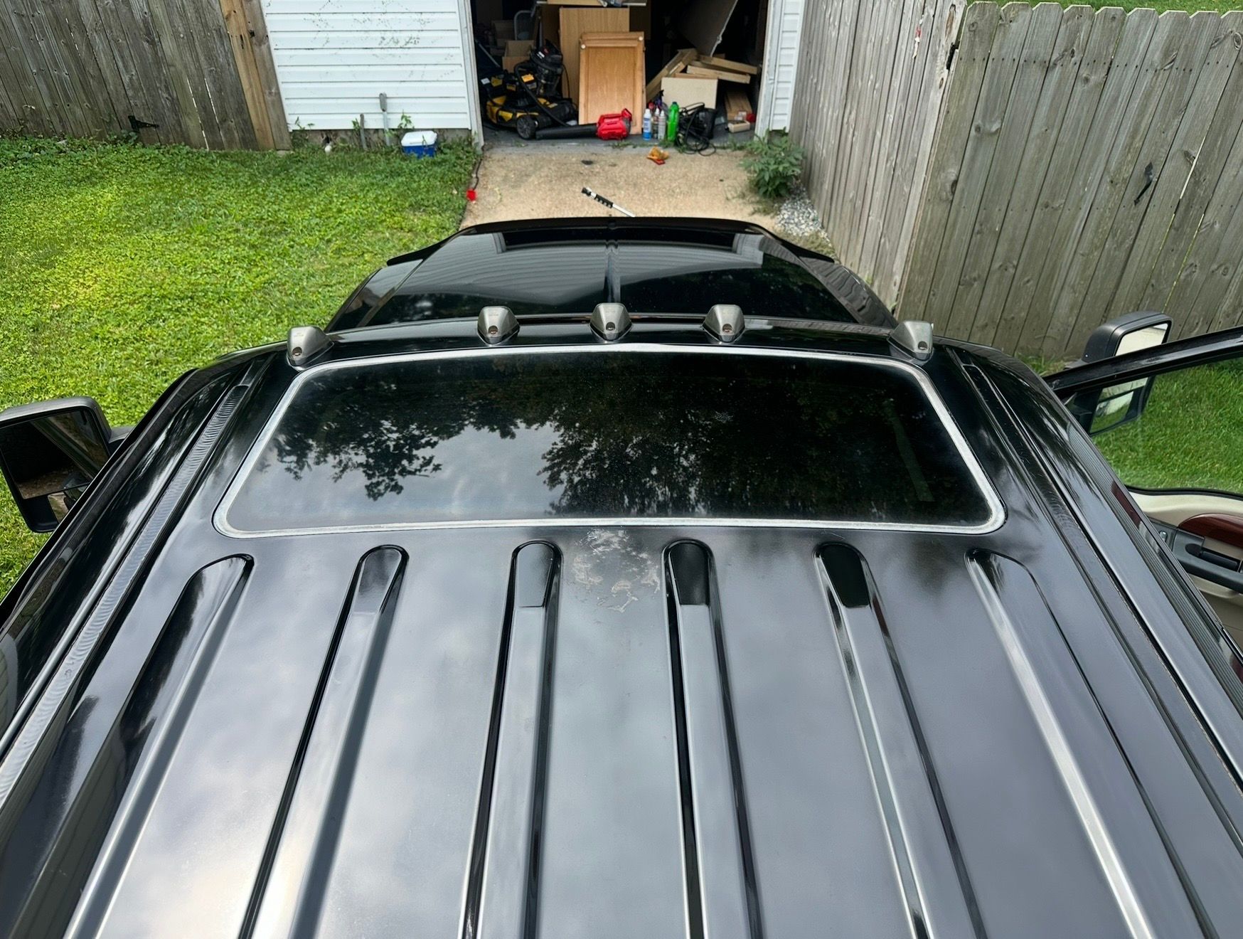 Overhead view of a black vehicle roof with open sunroof in a driveway near a garage