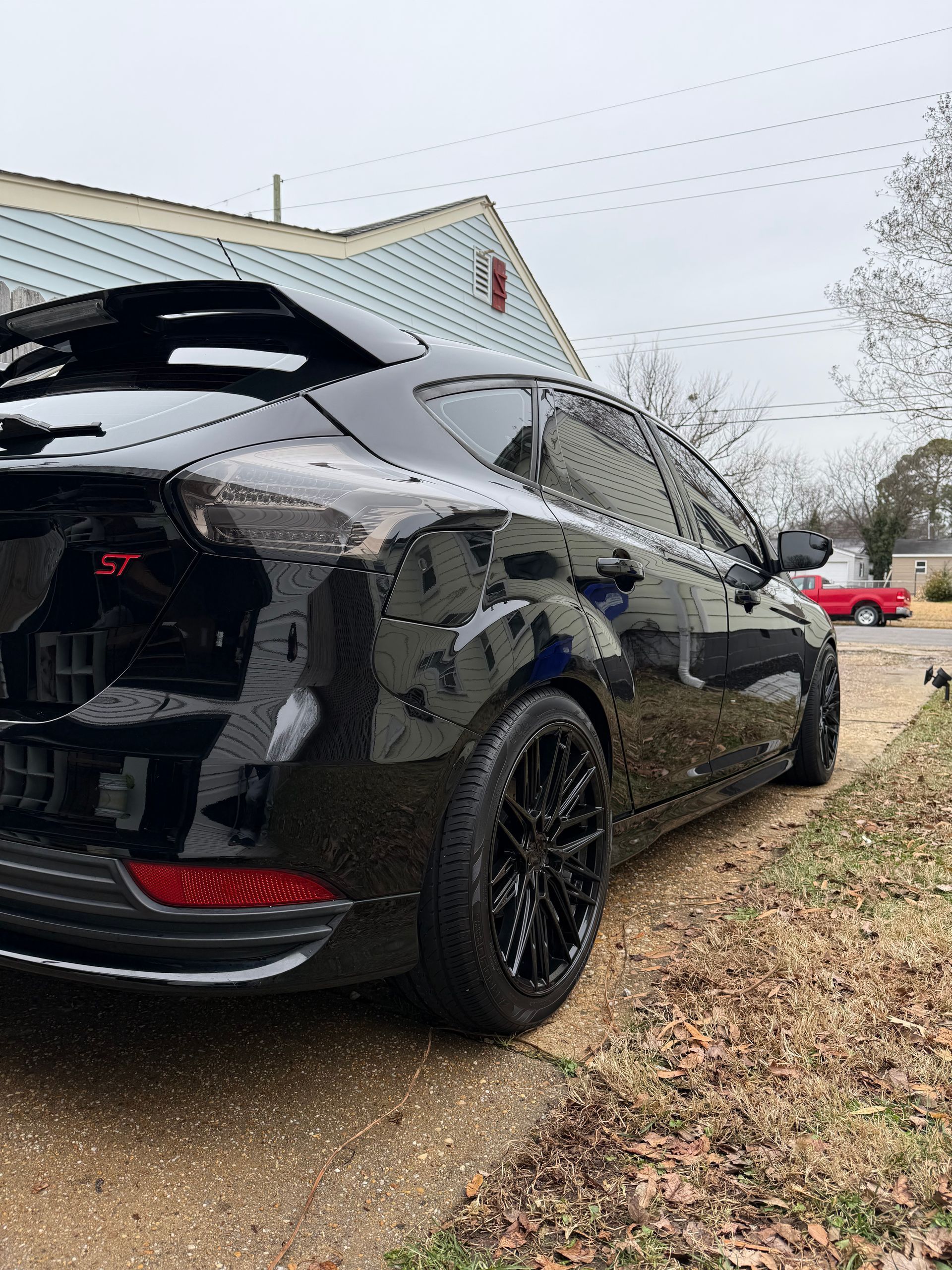 Black sports car parked beside a house on a wet driveway, rear and side view