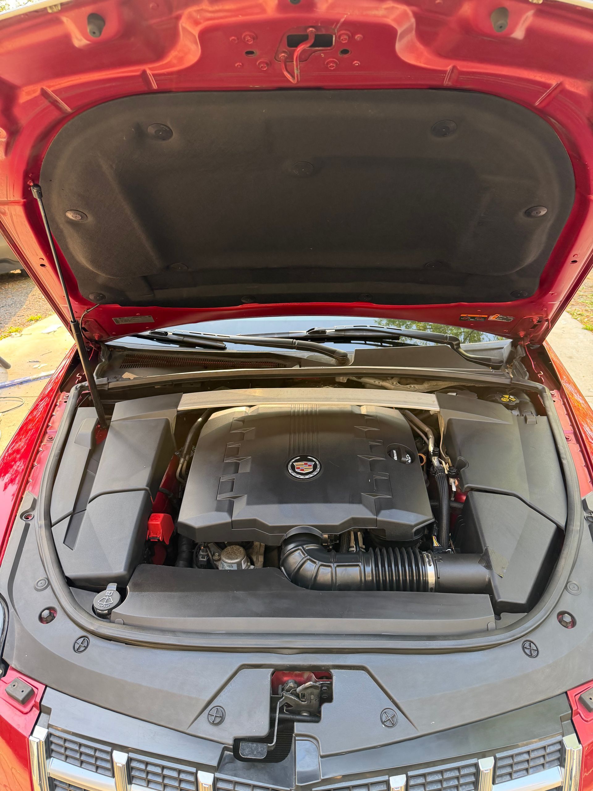Open car trunk with the engine compartment exposed, showing a black engine cover and red body panels.