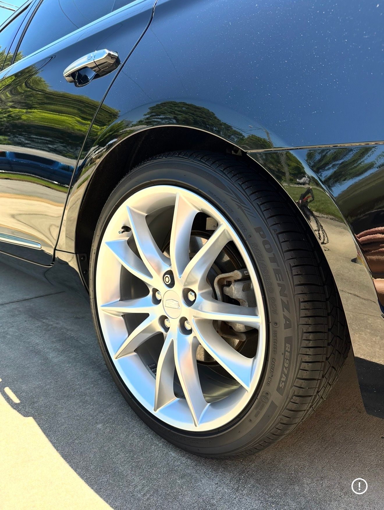 Close-up of a black car’s rear wheel and silver alloy rim in sunlight