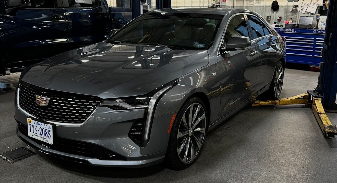 Gray Cadillac sedan in a workshop bay, parked beside a blue tool cart and car lift.