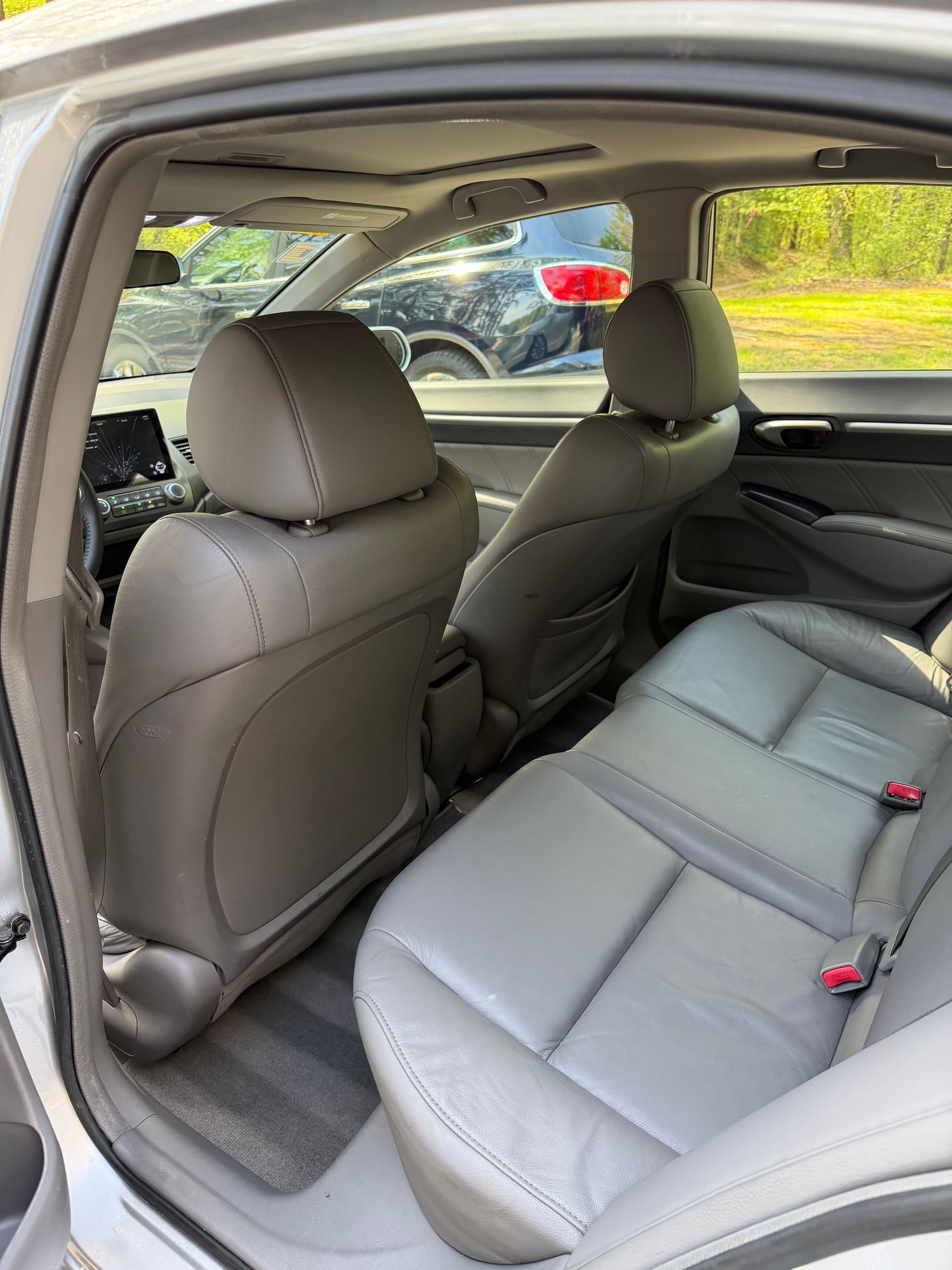 Car interior with gray rear seats and a tan front seat, viewed from the open back door