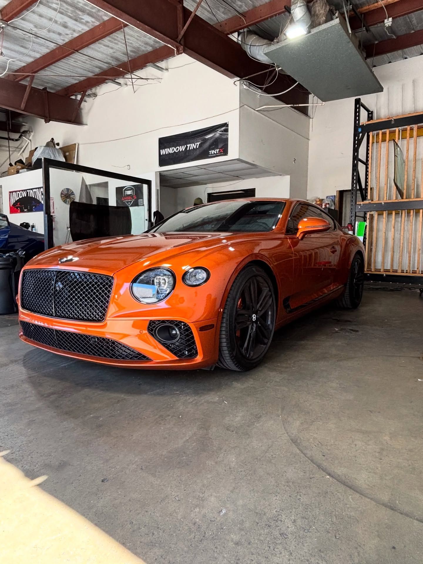 Orange Bentley coupe in a shop with black accents.