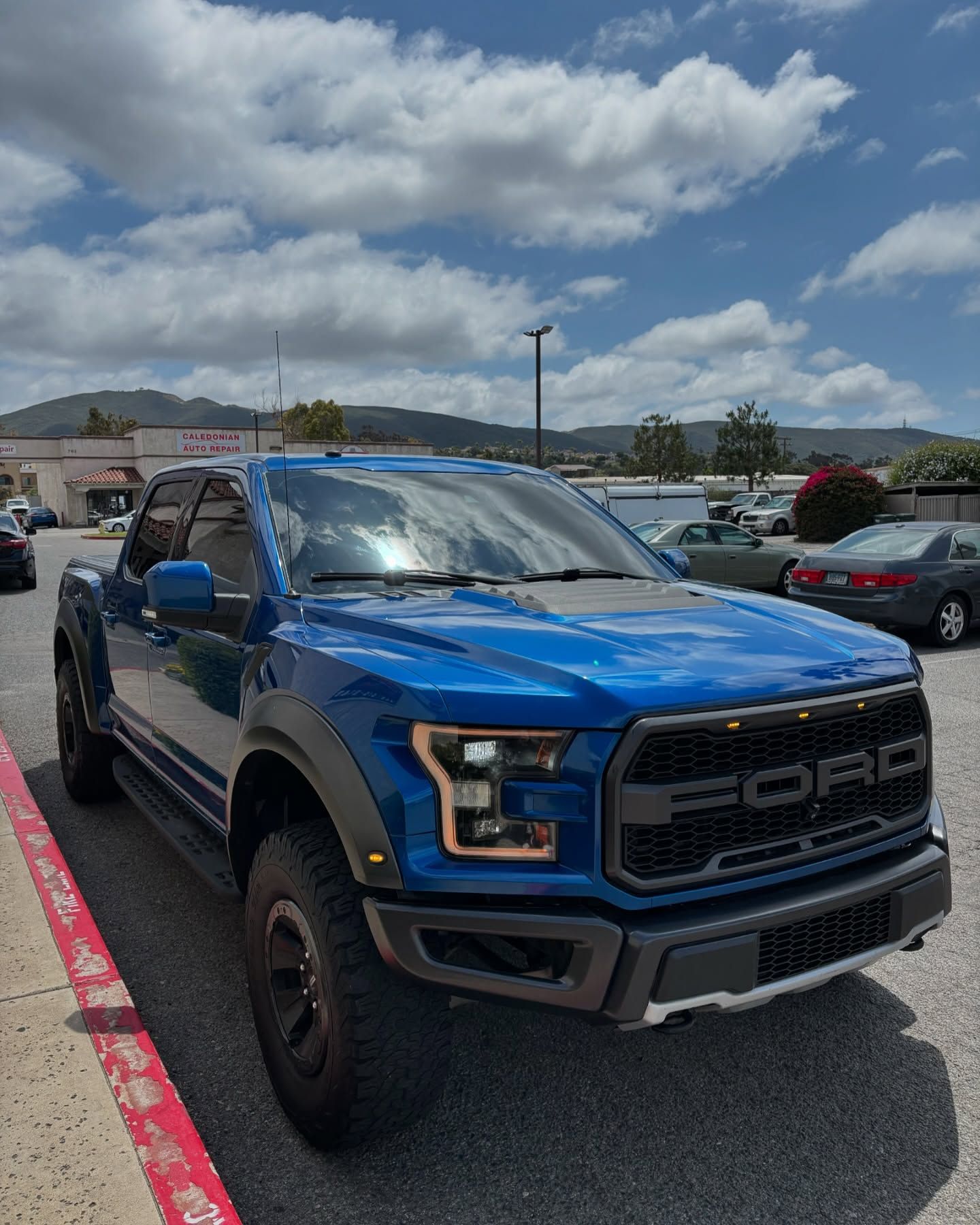 Blue Ford Raptor pickup truck parked in a lot under a cloudy sky.