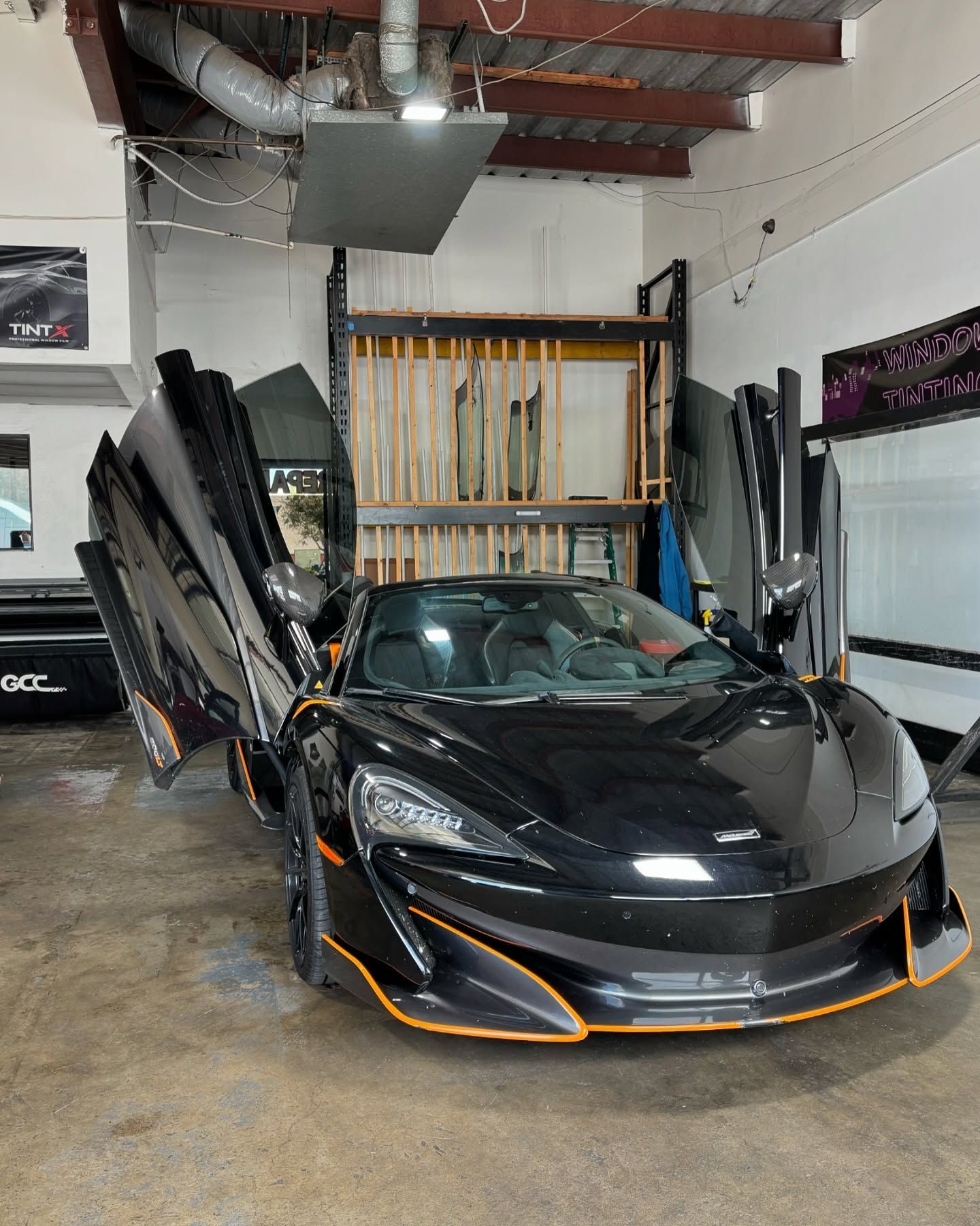 Black McLaren sports car with doors open in a garage, orange accents.