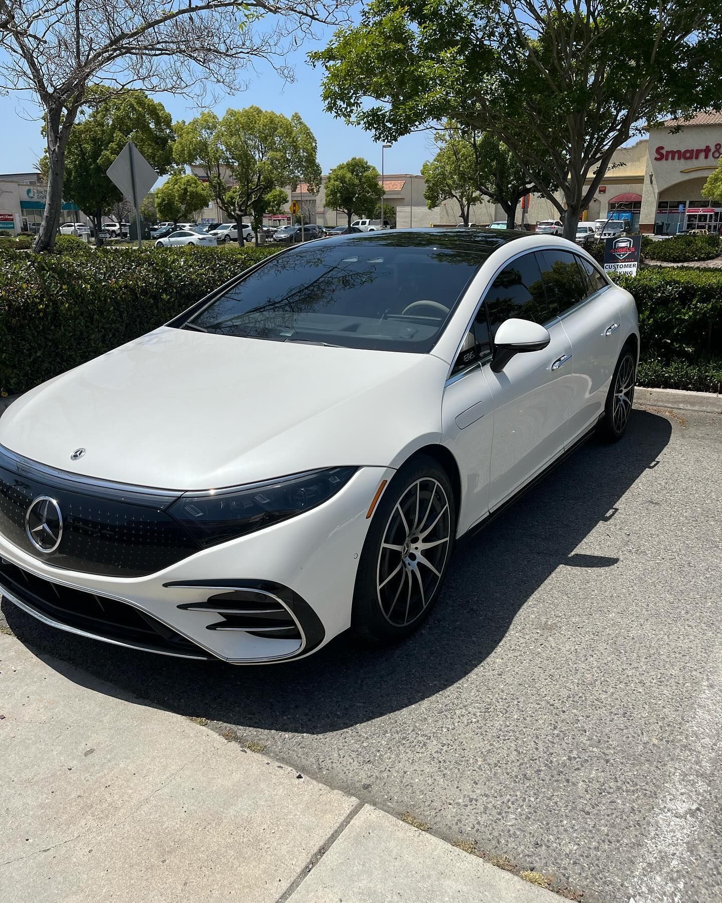 White Mercedes-Benz EQS sedan parked outside a strip mall with a blue sky and trees.