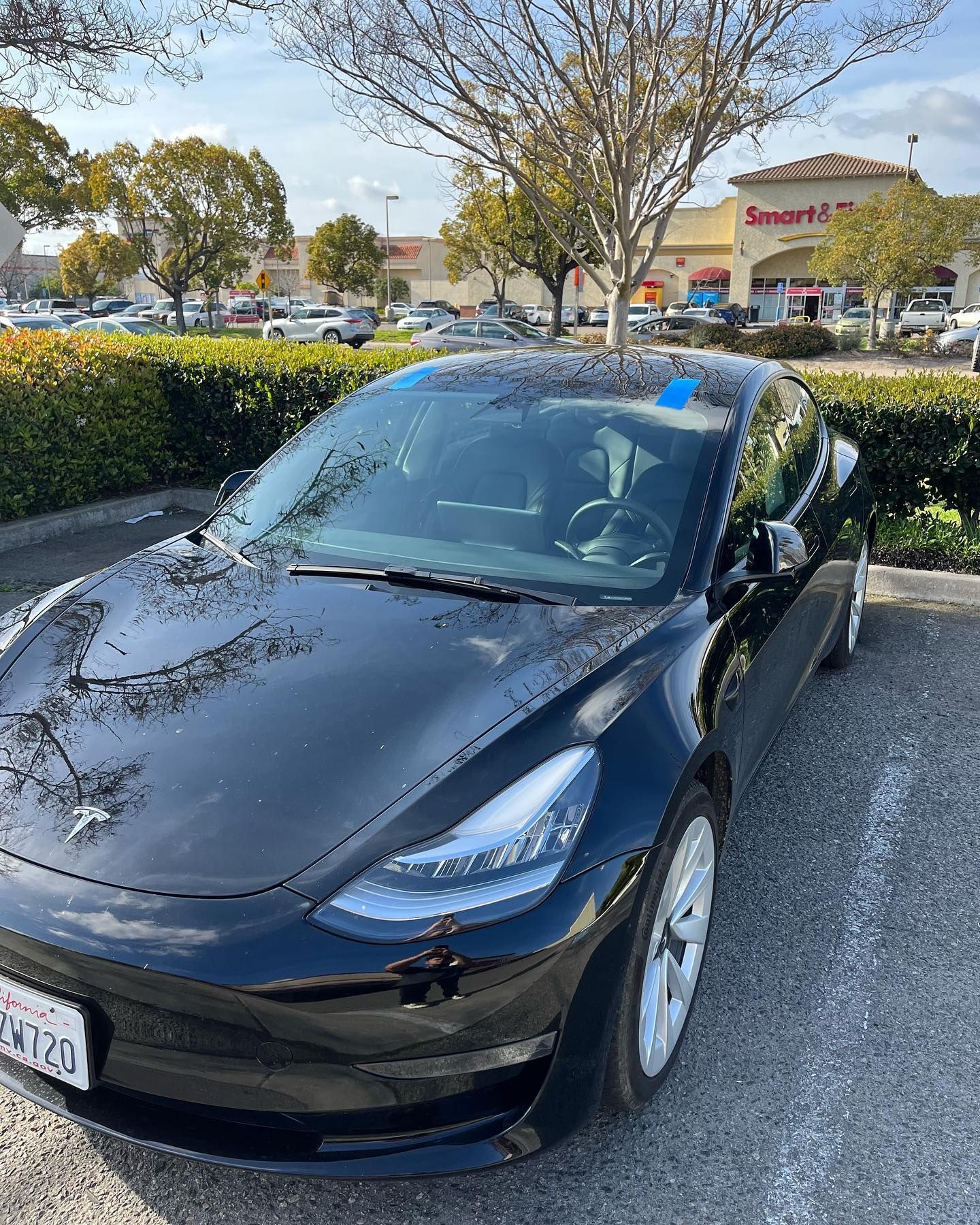 Black Tesla car parked in a lot, with a Smart & Final store in the background. Sunny day.