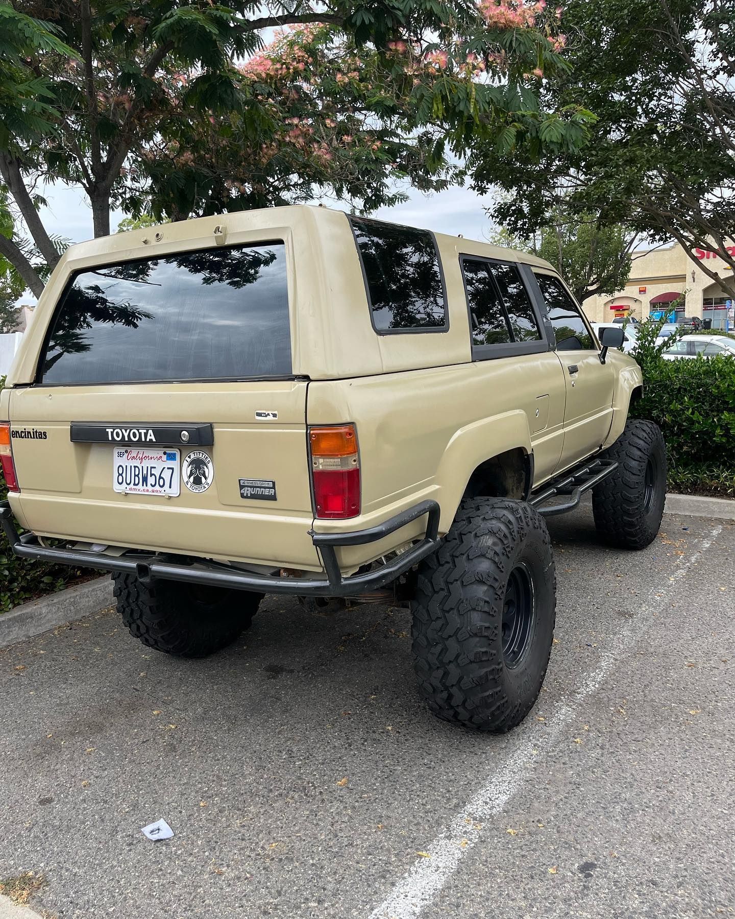 Tan Toyota 4Runner with large tires, parked on pavement, rear view.