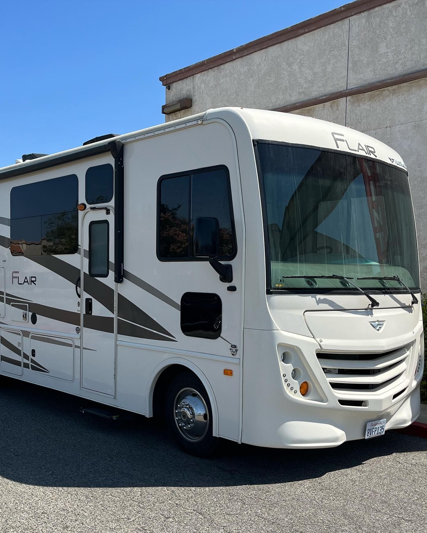 White Flair RV parked in front of a building on a sunny day.