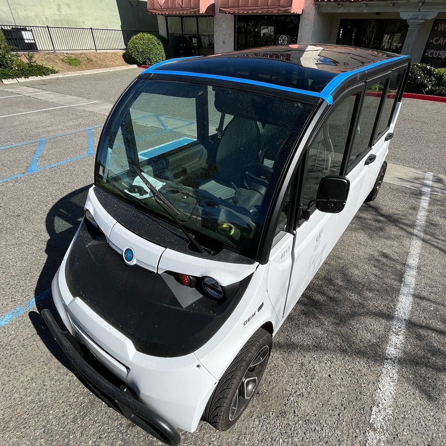 White GEM electric vehicle parked in a parking lot. Blue roof trim.