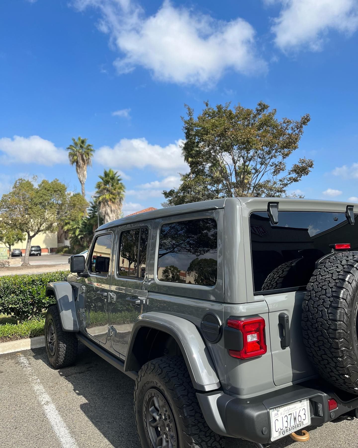 Gray Jeep Wrangler parked on a sunny day, palm trees in the background.