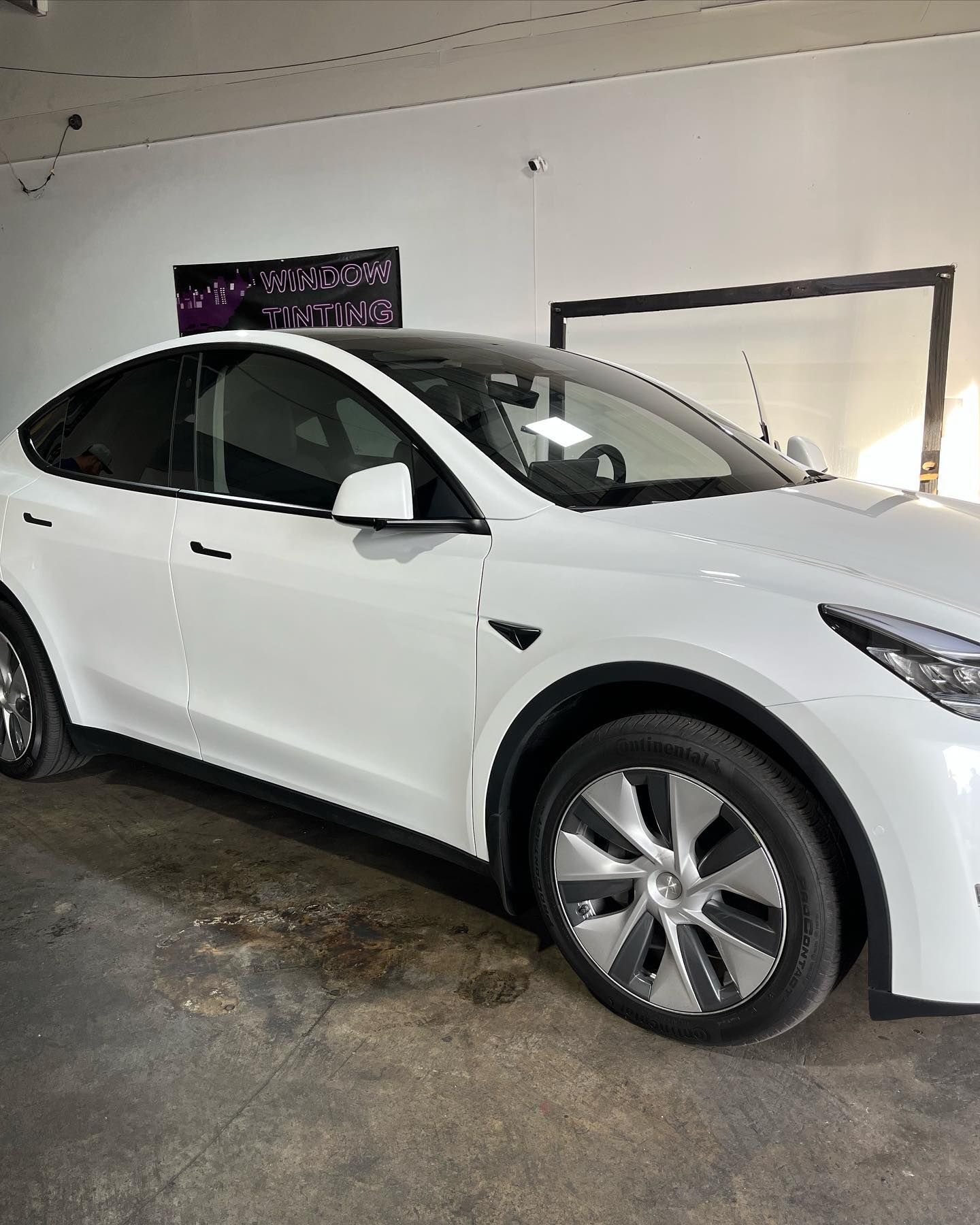 White Tesla Model Y car in a garage with tinted windows.