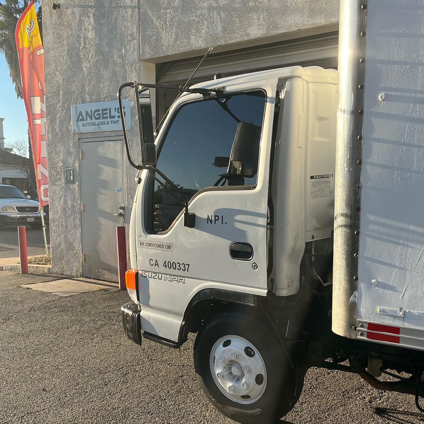 White box truck parked next to a building, with the name 