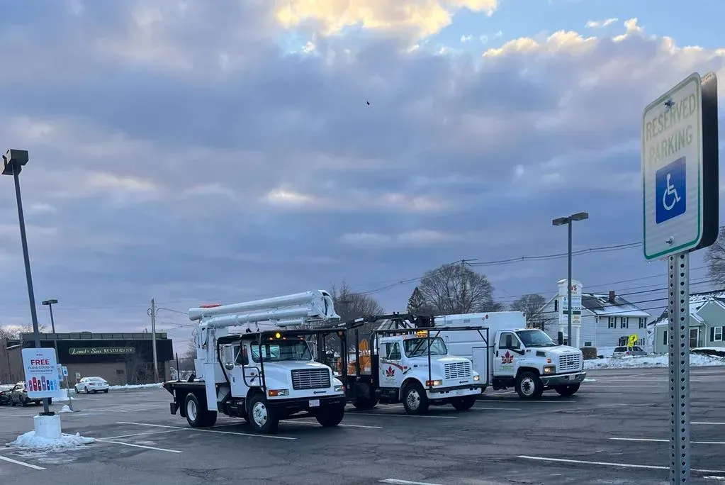 Three white utility bucket trucks parked in a paved parking lot under a cloudy sky, near an accessible parking sign.