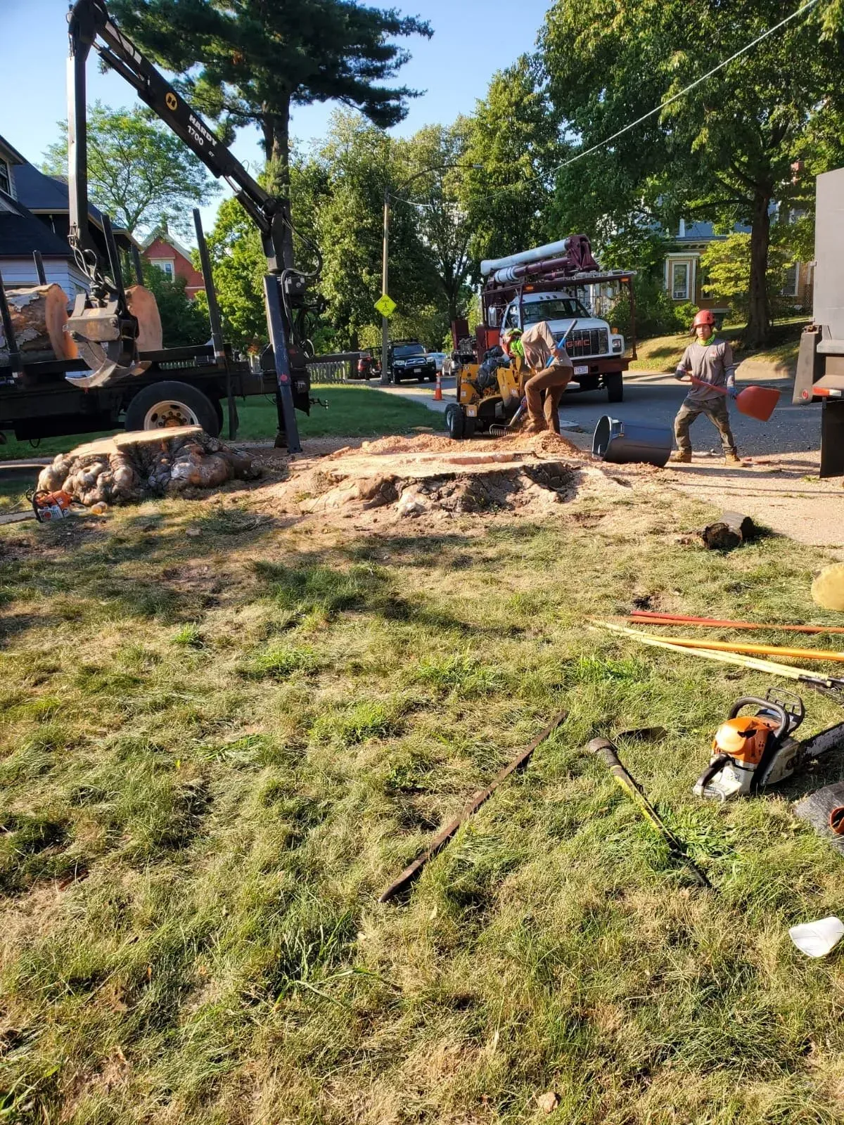 A work crew clears a felled tree with a boom truck and wood chipper in a residential yard.