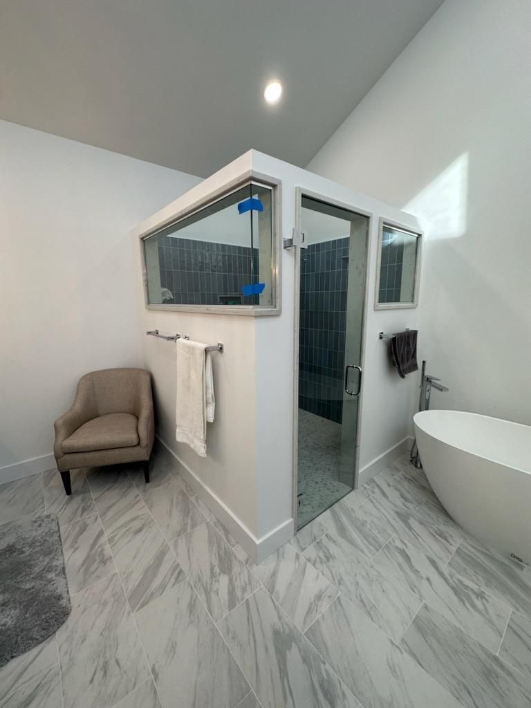 A bathroom with a tub , chair , and mirror.