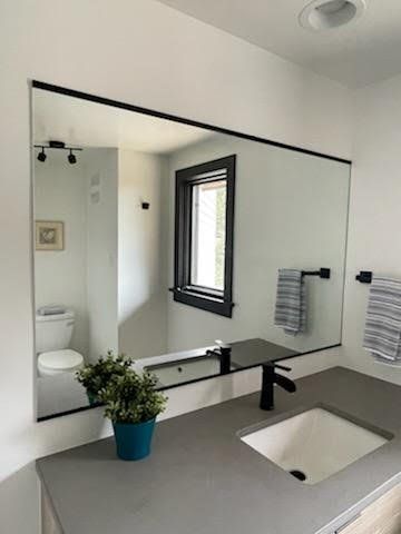 A bathroom with a large mirror , sink , toilet and window.