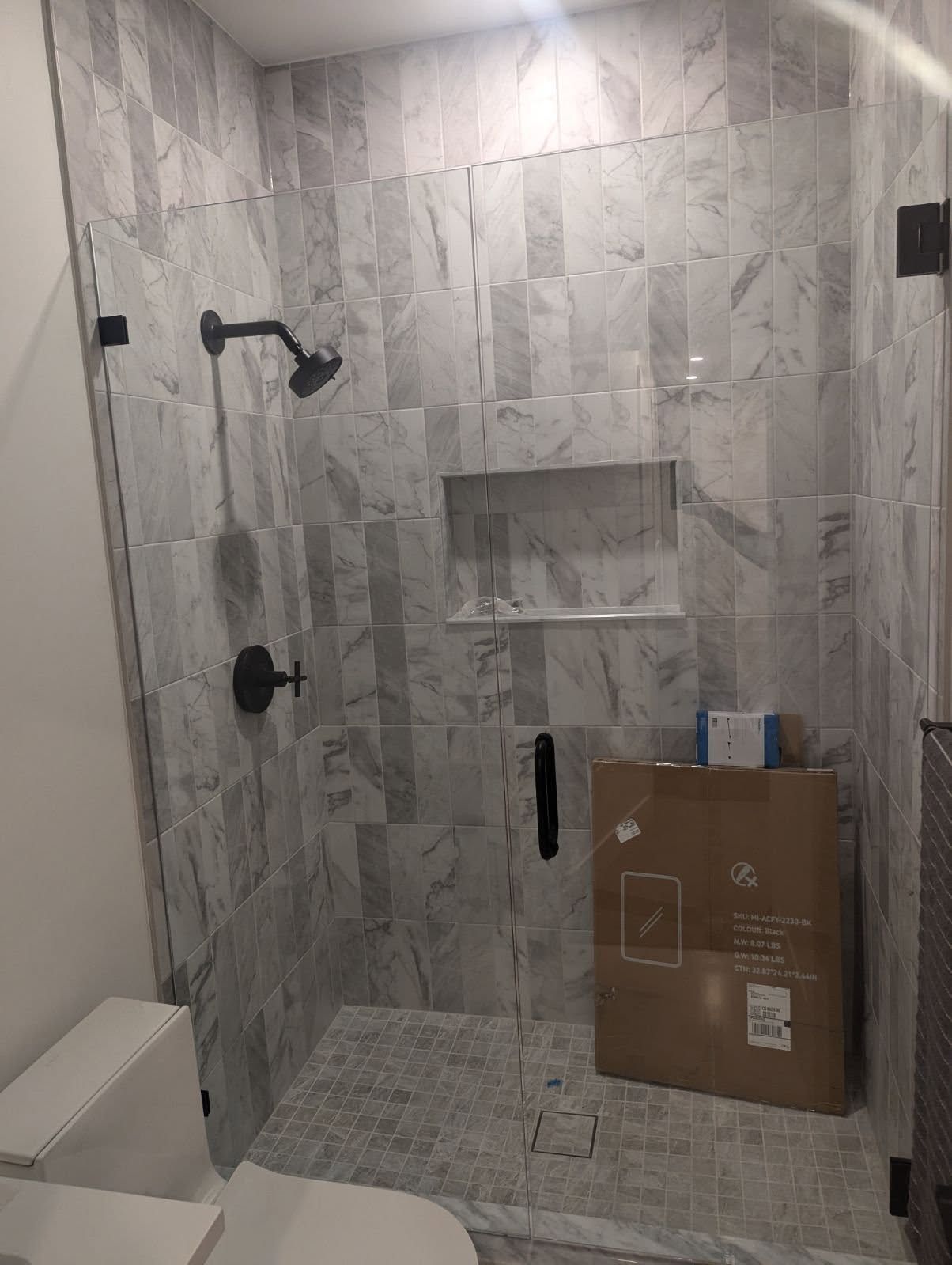 A bathroom with a walk in shower , toilet , and box on the floor.