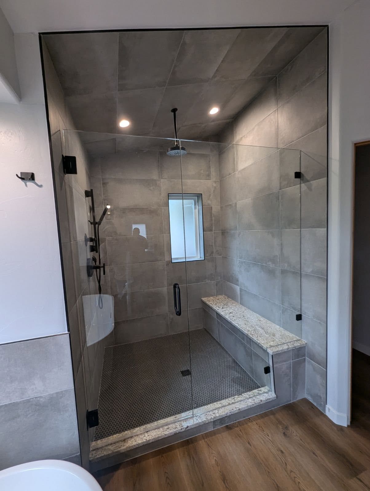 A bathroom with a walk in shower with a glass door and a bench.