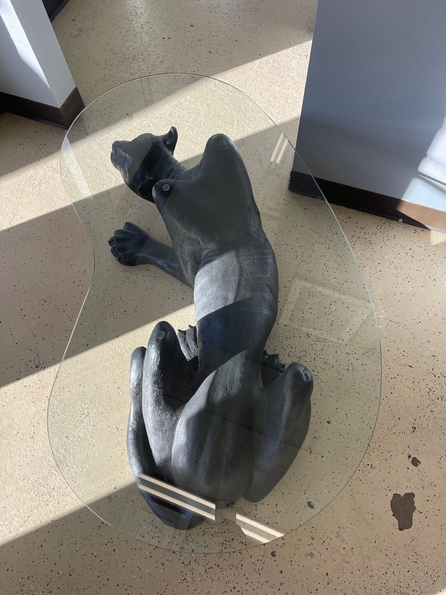 A statue of a cat is sitting on a glass table.