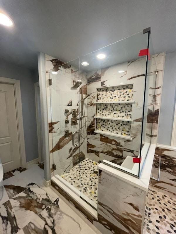 A bathroom with a walk in shower with a glass door and shelves.
