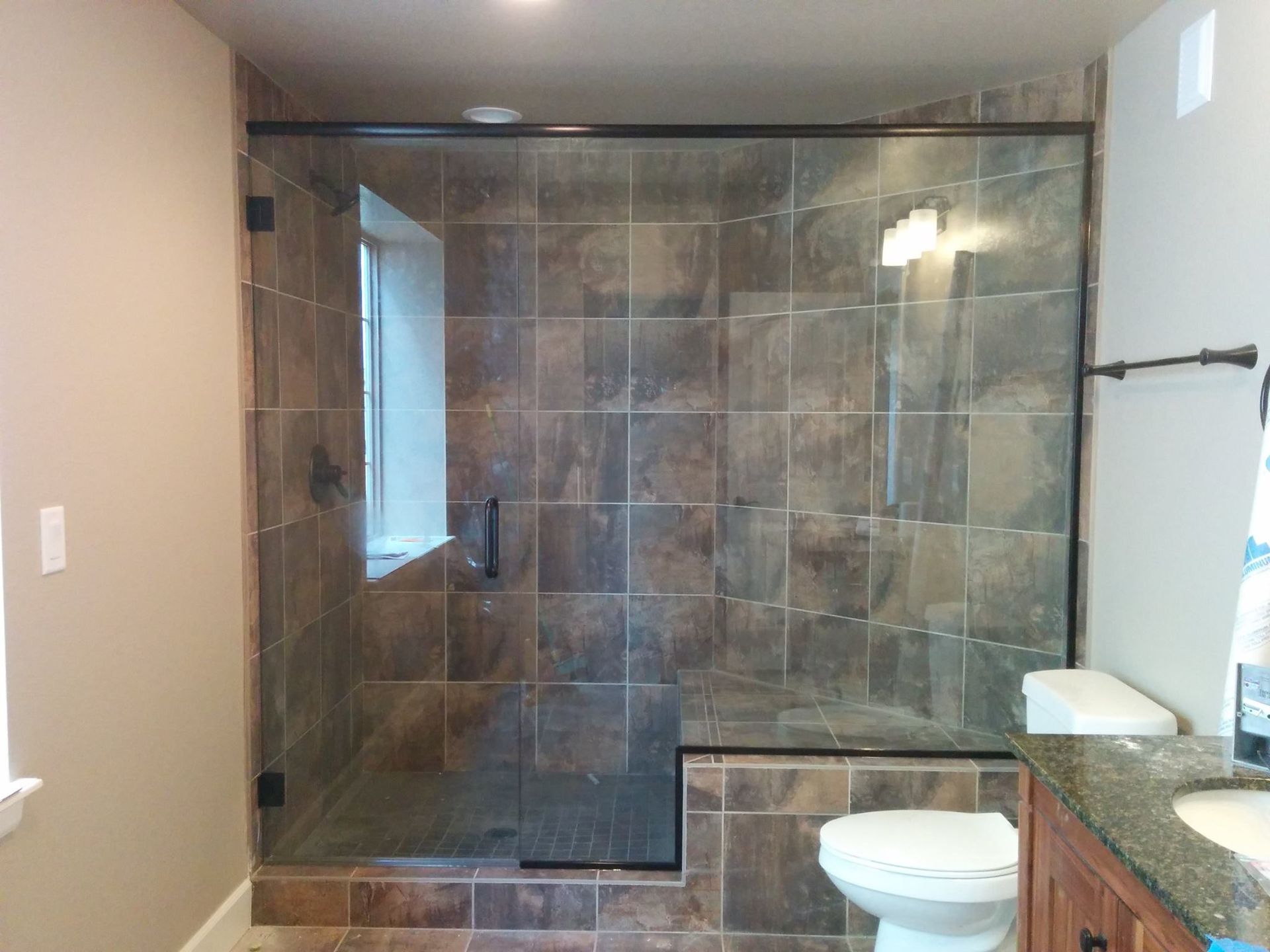 A bathroom with a walk in shower , toilet , sink and window.