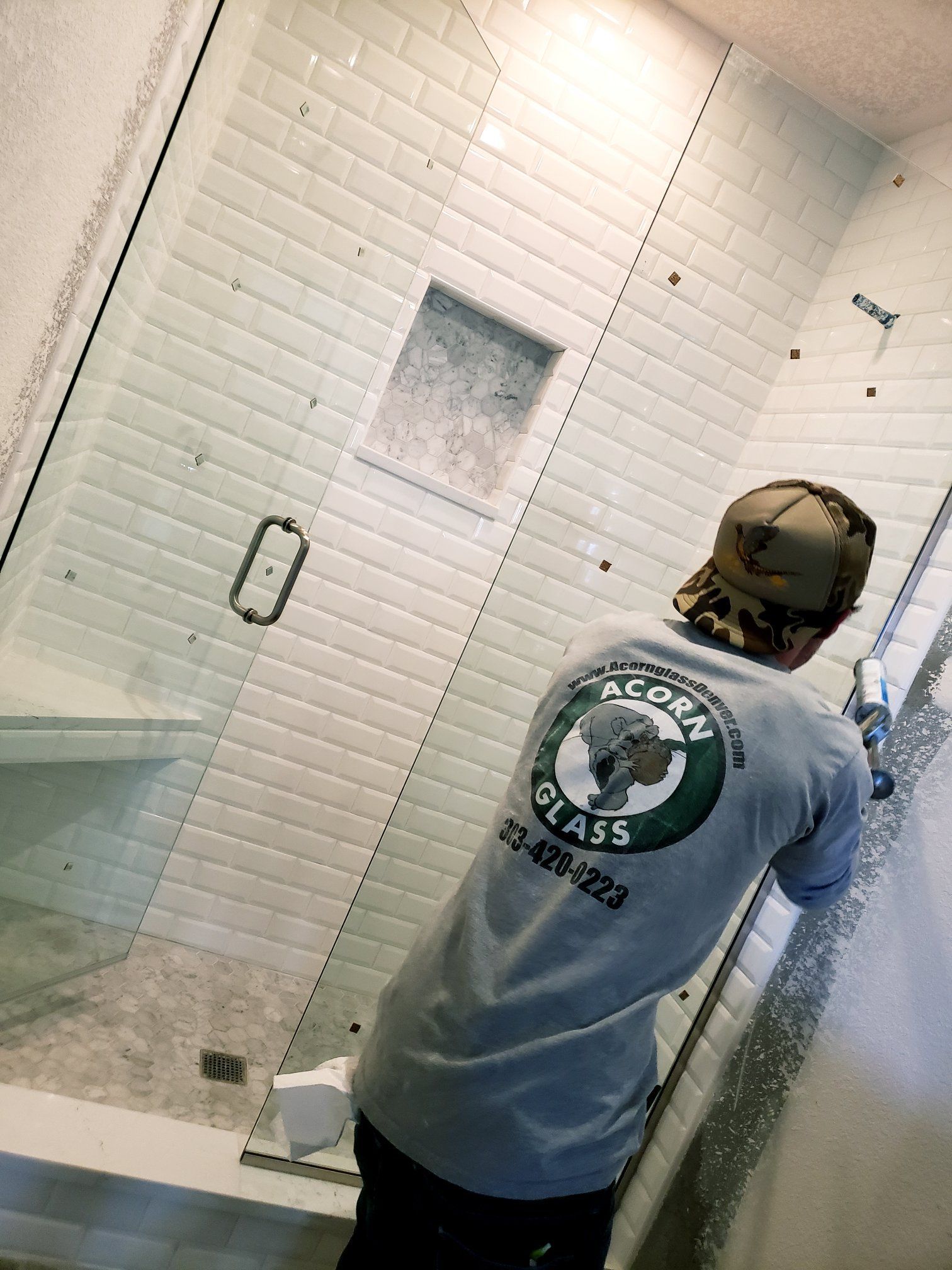 A man is working on a shower door in a bathroom.