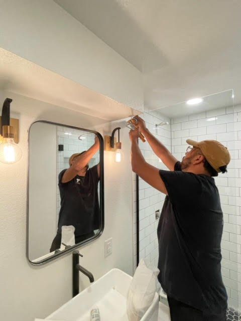 A man is installing a light fixture in a bathroom.
