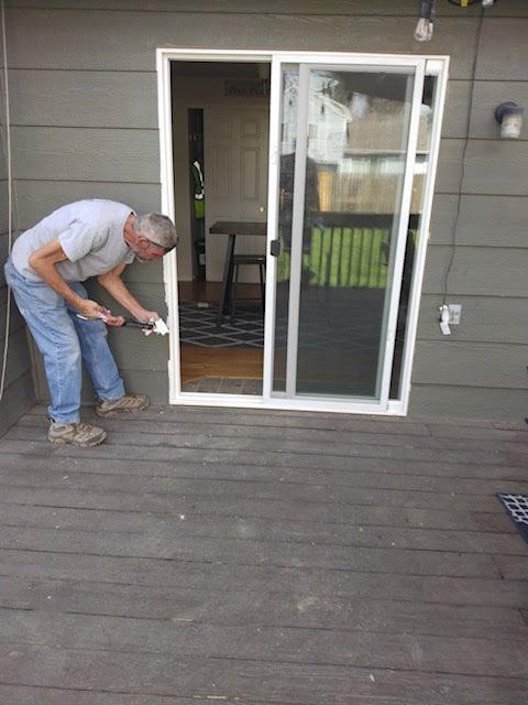 A man is painting a sliding glass door on a deck