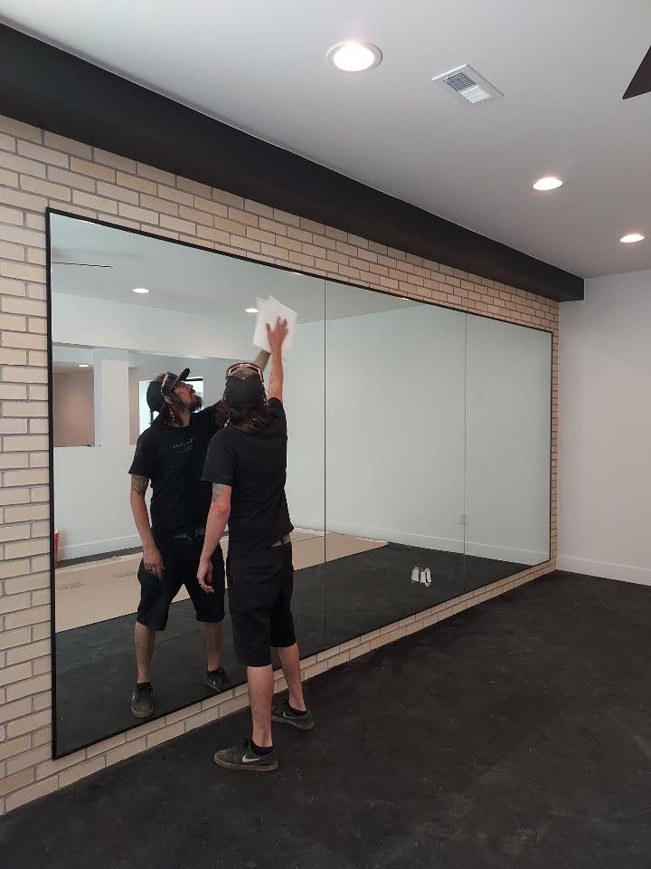 A man is cleaning a large mirror in a gym.