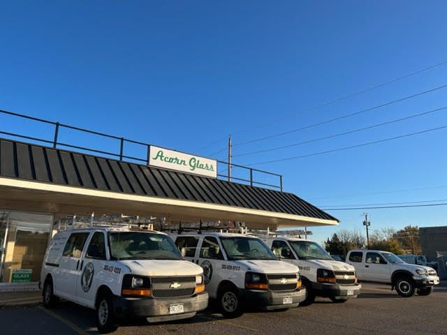 A row of white vans parked in front of a building that says acorn glass