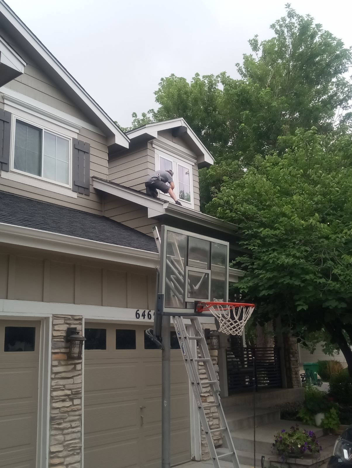 A man is standing on the roof of a house next to a basketball hoop.