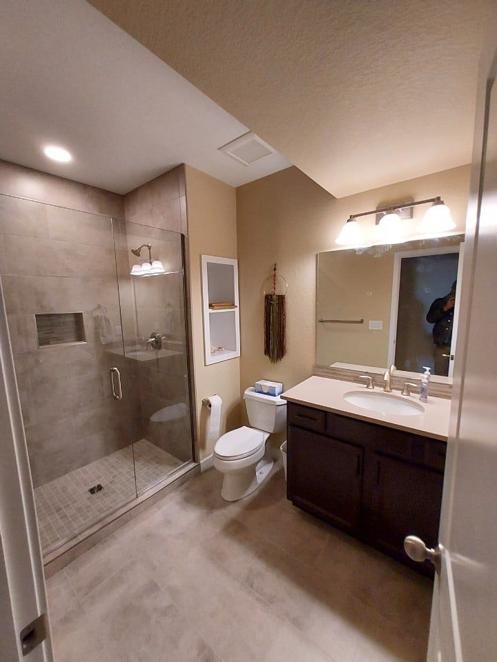 A bathroom with a toilet , sink , shower and mirror.