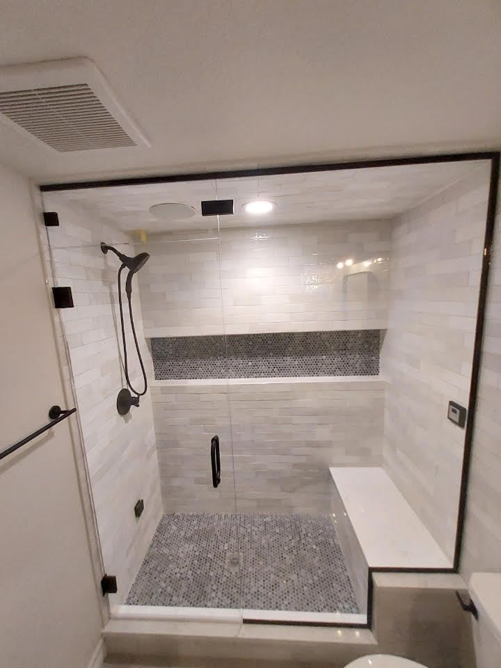 A bathroom with a walk in shower with a glass door and a bench.