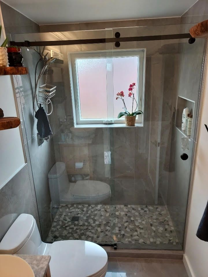A bathroom with a toilet , shower , and window.