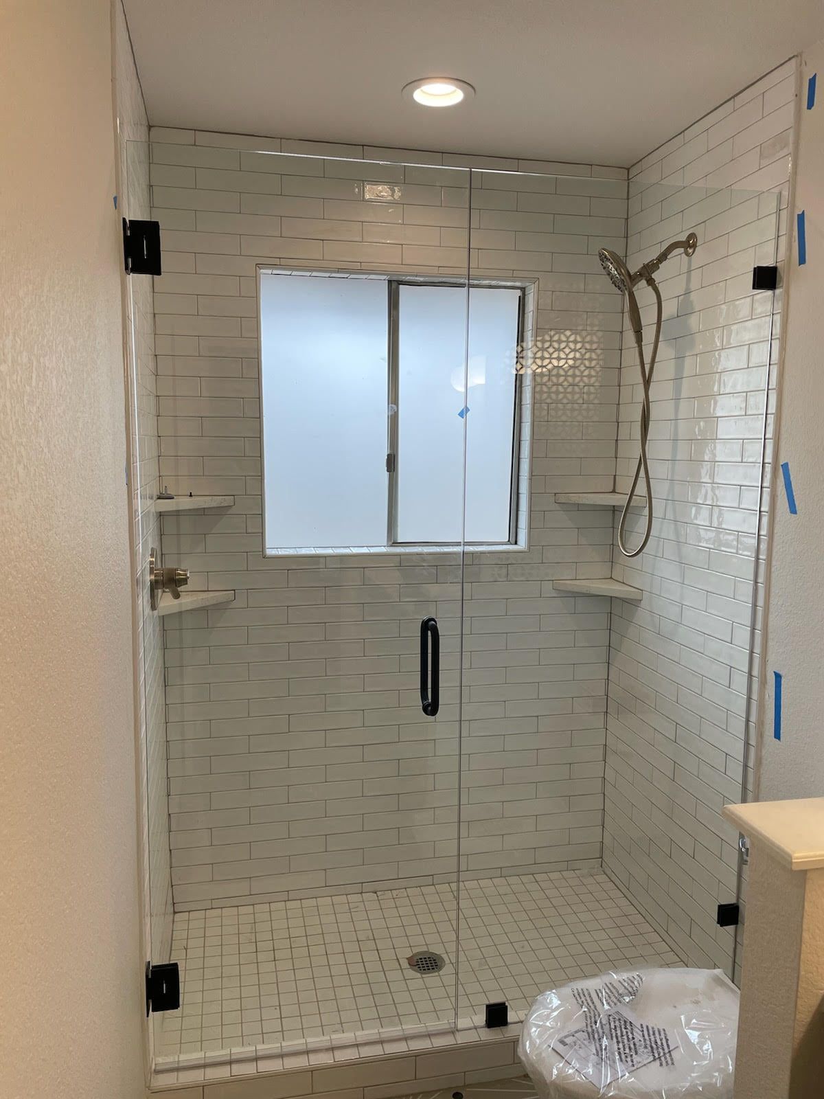 A bathroom with a walk in shower with a glass door and a window.