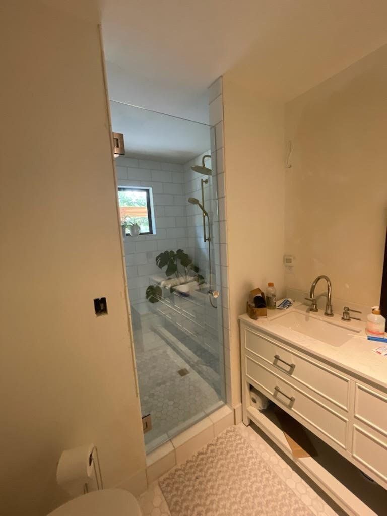 A bathroom with a walk in shower , sink , toilet and mirror.