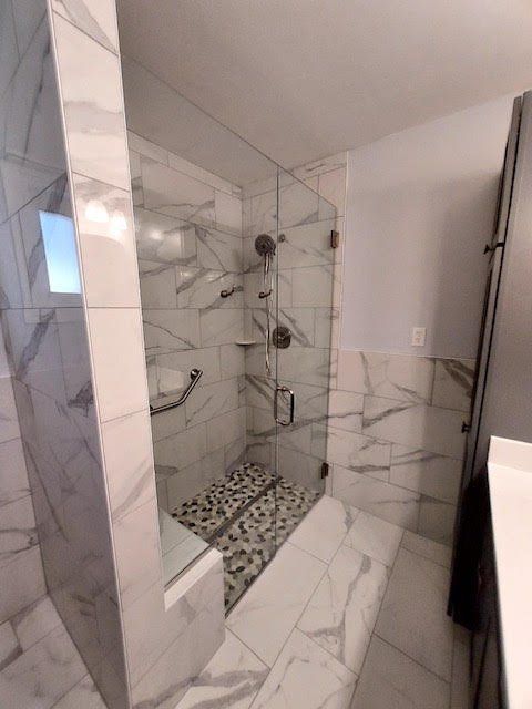 A bathroom with marble tiles and a walk in shower with a glass door.
