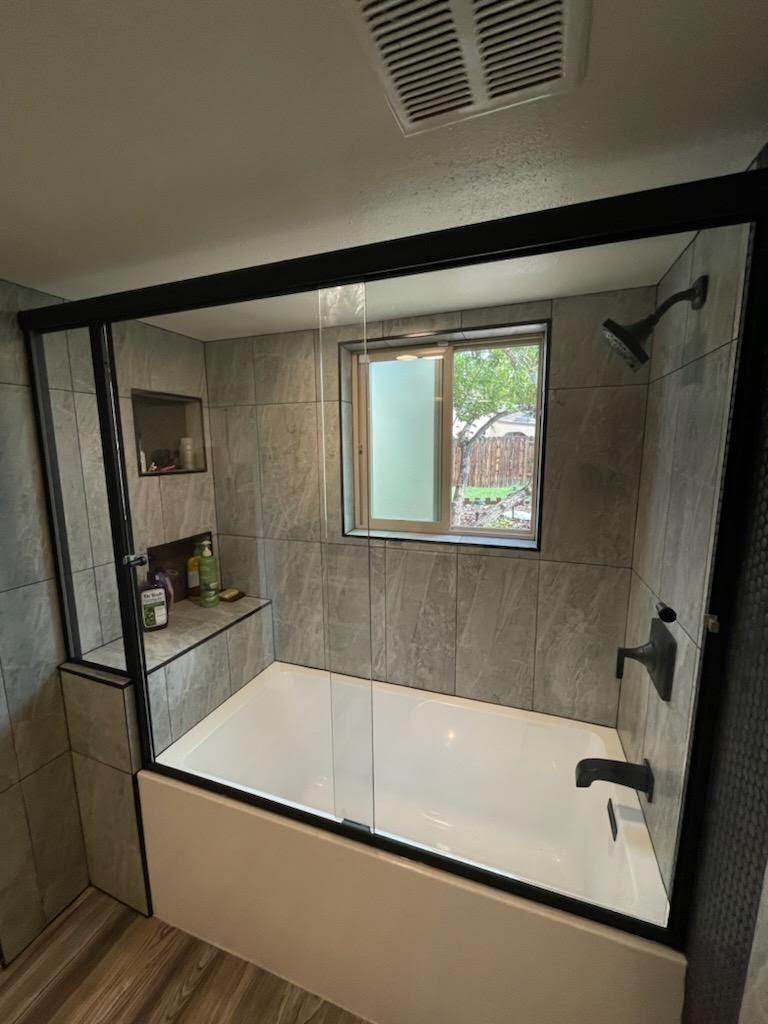 A bathroom with a bathtub , shower , and window.