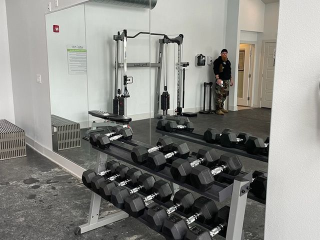 A man is standing in a gym next to a row of dumbbells.