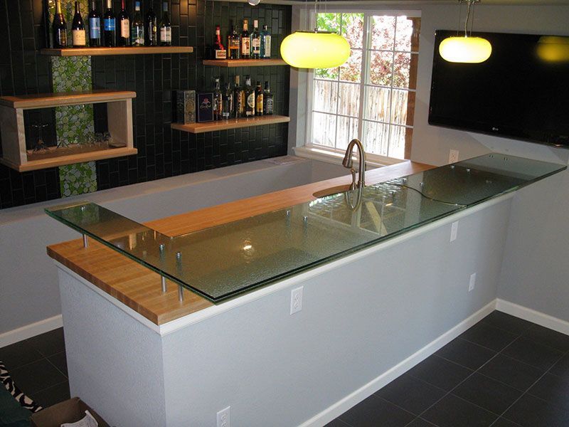 A kitchen with a glass counter top and bottles on shelves