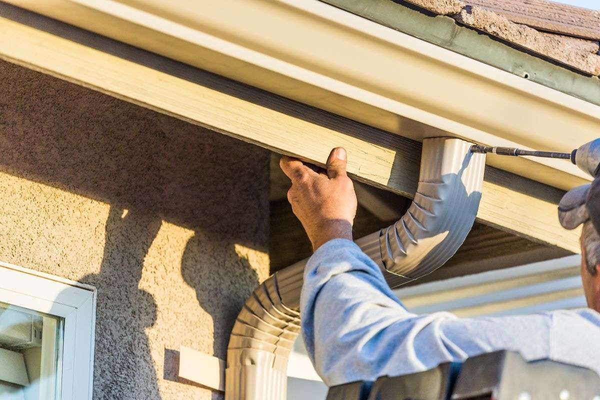 Worker installing a gutter on a house exterior with a power tool