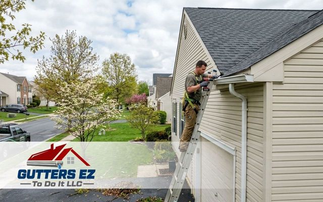 Worker cleaning gutters on a house roof beside a suburban lawn, with GUTTERS EZ logo overlay